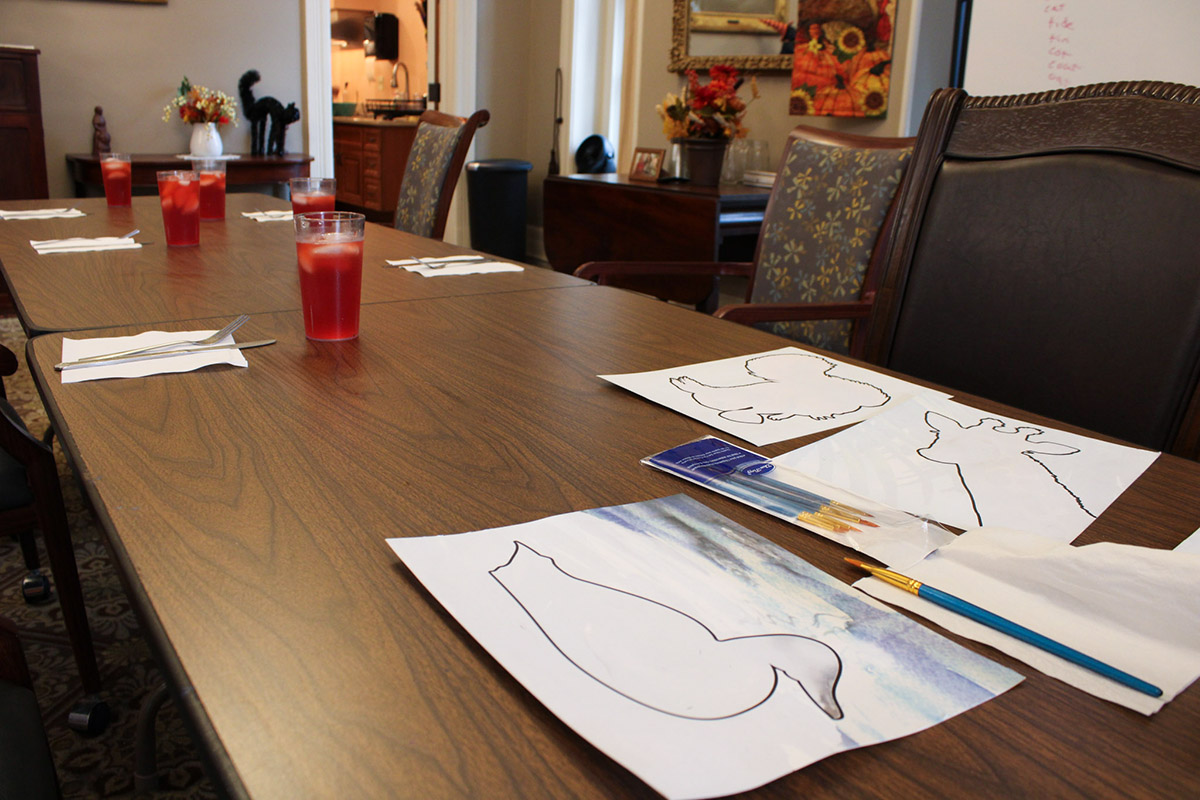 A watercolor painting activity for seniors at Vassar-Warner Home, set on a long table in the common area.
